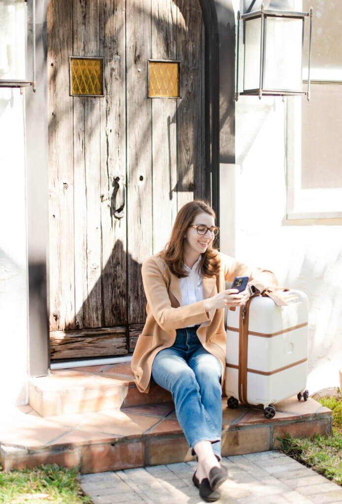 lauren, food allergy travel agent preparing for flight with food allergies wearing a tan sweater and sitting next to suitcase