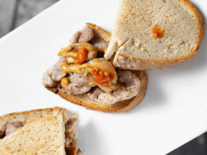 This is a traditional sandwich in Portugal made with marinated pork, bread, and a variety of toppings like egg, cheese, tomatoes, lettuce, and bacon.