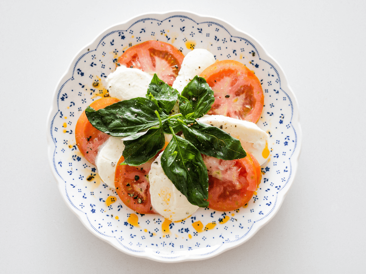 egg free lunch in Italy enjoying a caprese salad of basil, tomato, and cheese on blue and white plate