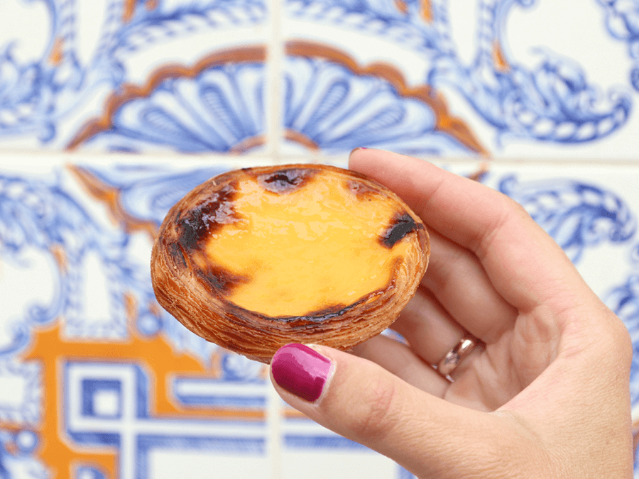 Traveling to Portugal With a Soy Allergy holding a Pastel de Nata next to blue patterned wall.