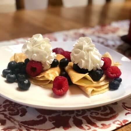 a plate of crepes with berries and whipped cream while eating nute free in france.