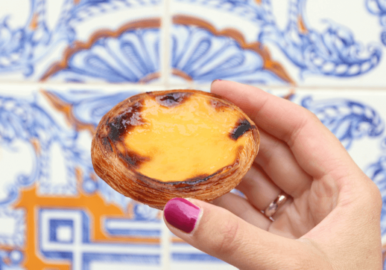 Traveling to Portugal With a Soy Allergy holding a Pastel de Nata next to blue patterned wall.